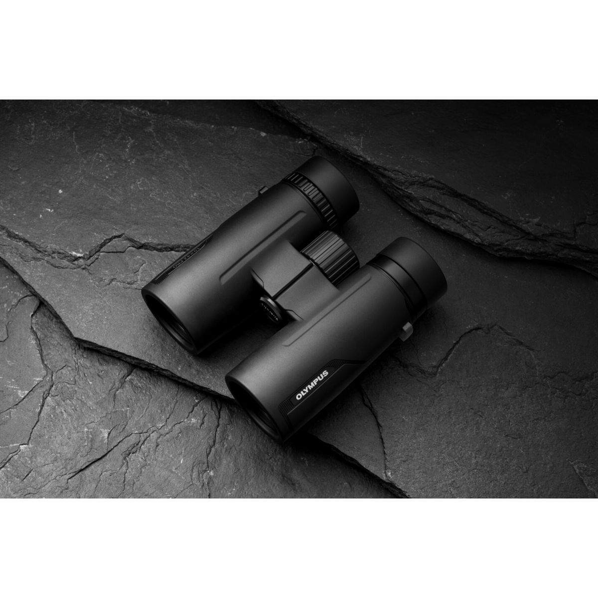 Czarna lornetka Olympus leży na ciemnej, teksturowanej powierzchni. Widoczna nazwa marki.