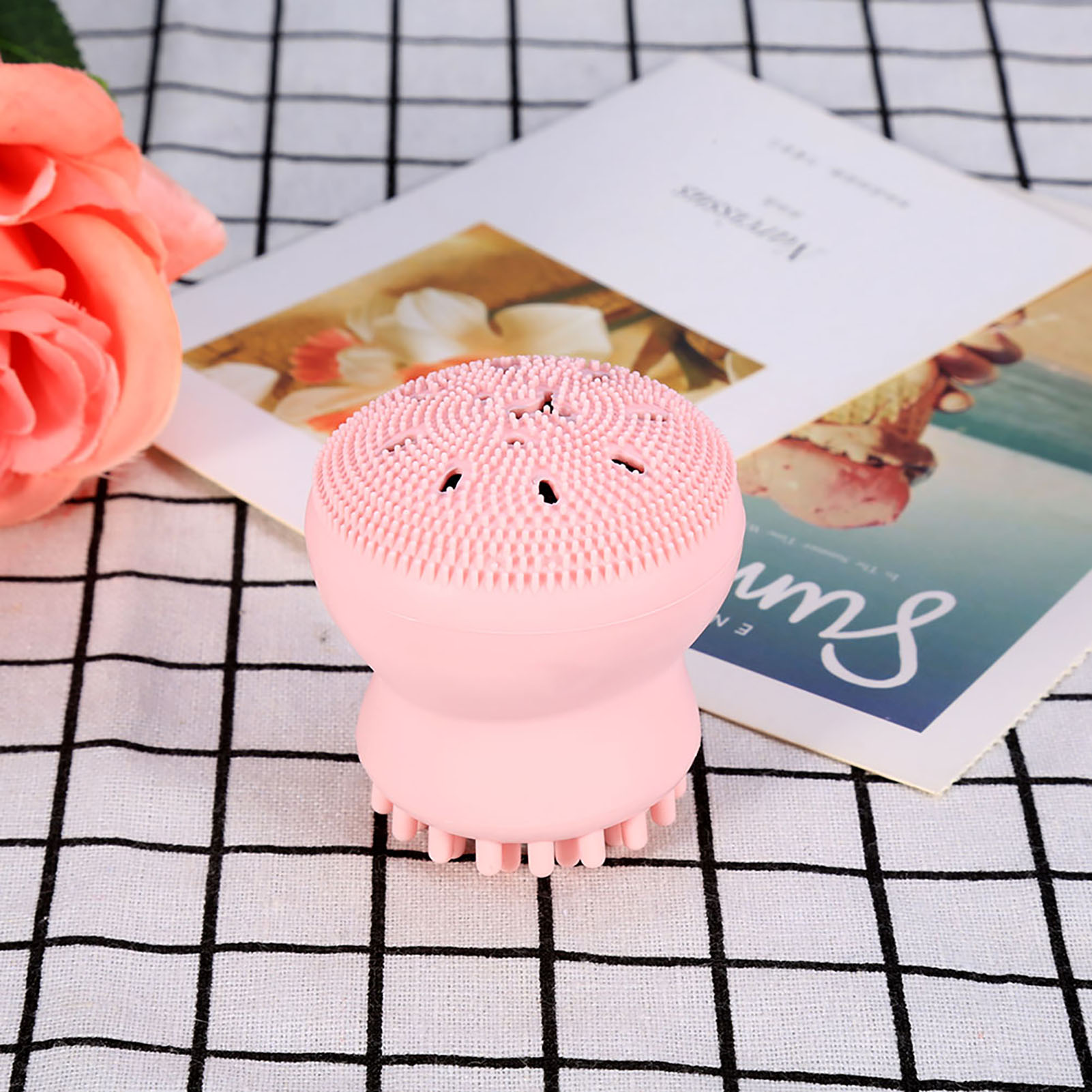 Eine rosa, oktopusförmige Gesichtsreinigungsbürste auf einer karierten Oberfläche.