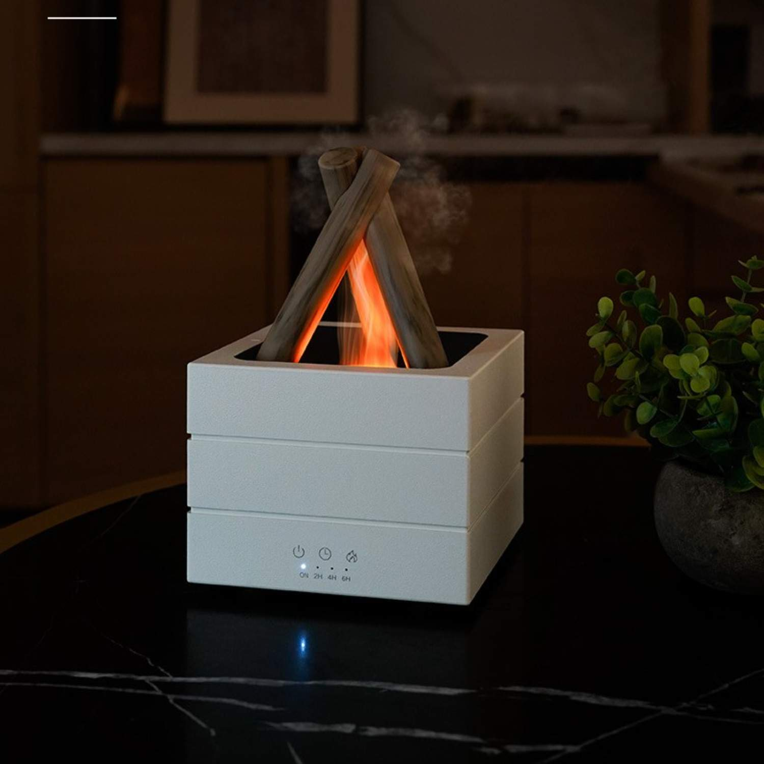 Ein weißer Aroma-Diffusor steht auf einem Tisch und verströmt einen Nebel mit Holzscheiten und einem Flammeneffekt.