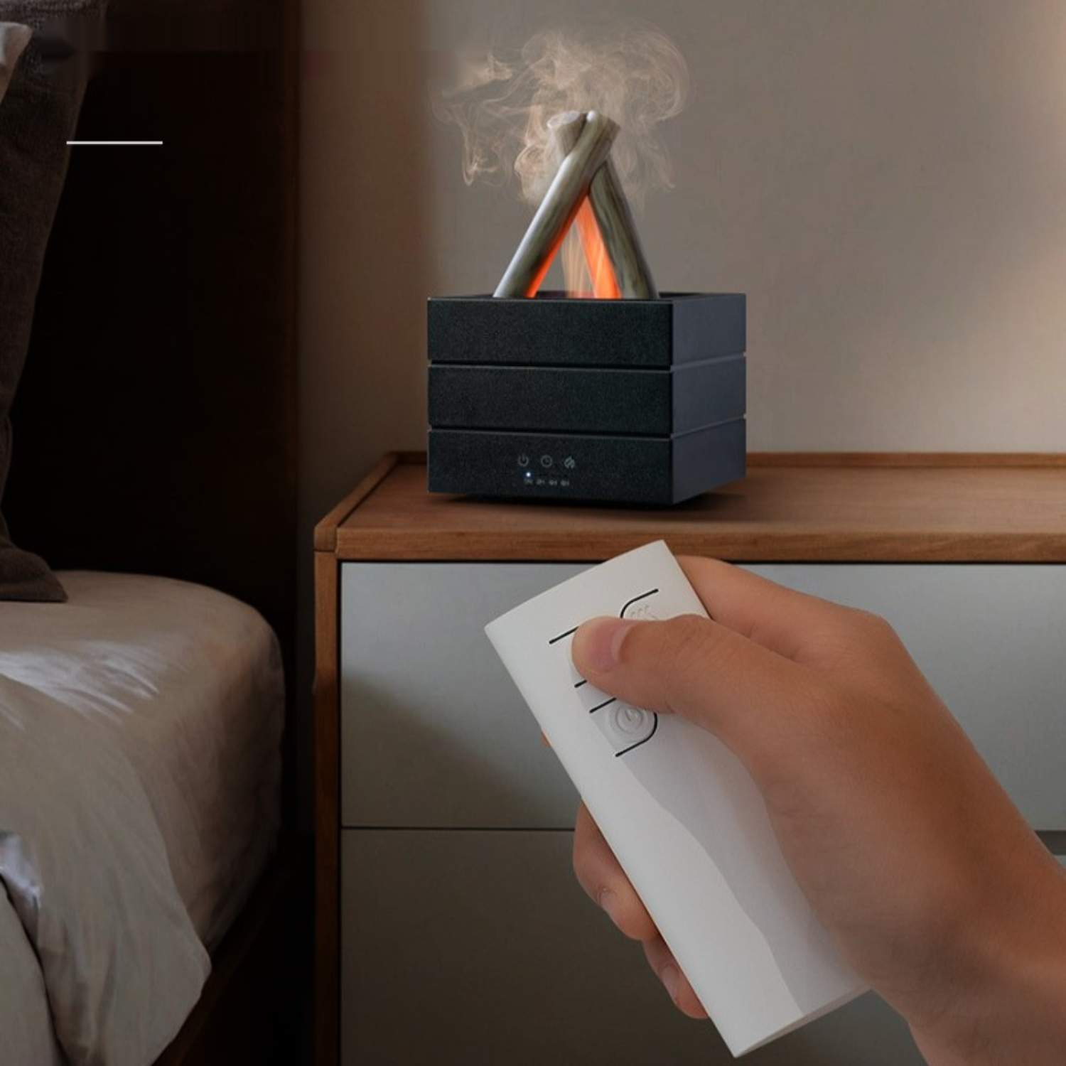 Eine Hand hält eine Fernbedienung, die auf einen schwarzen Aroma-Diffusor auf einem Nachttisch gerichtet ist.