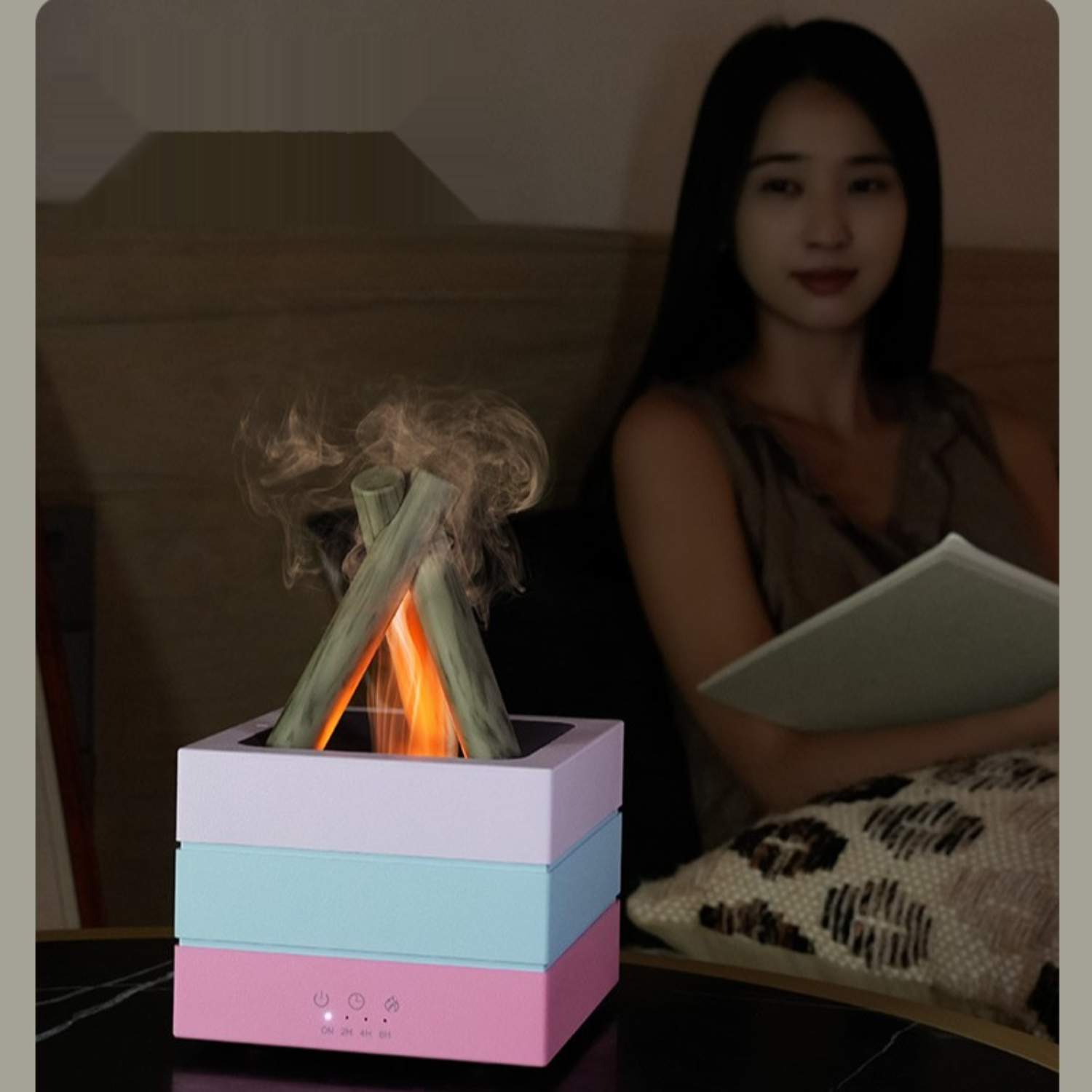 Eine Frau sitzt in der Nähe eines beleuchteten Lagerfeuer-förmigen Geräts. Das Gerät hat eine rosa, blaue und hellfarbene Basis.