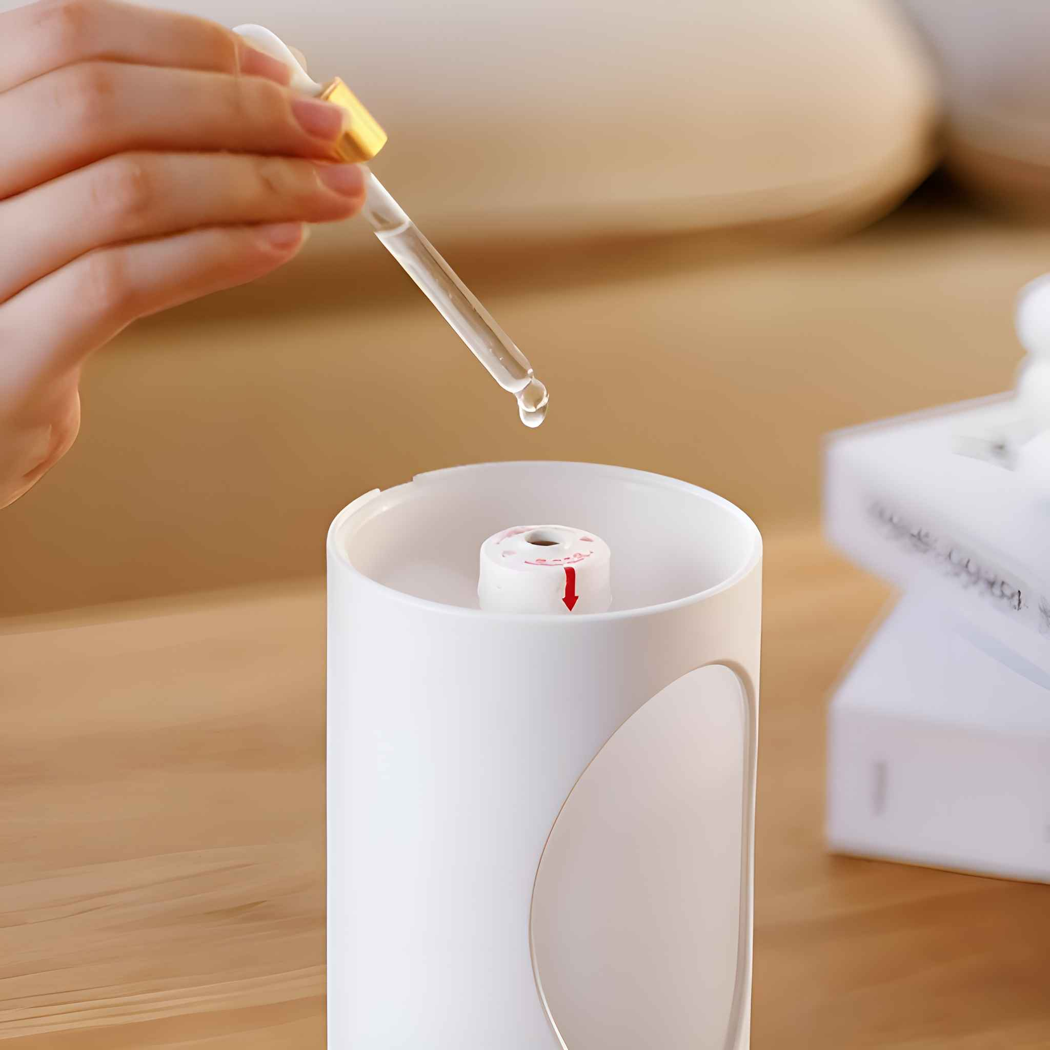 Eine Hand, die eine Pipette hält, mit einem Flüssigkeitstropfen, der in einen weißen Diffusor fallen soll. Roter Pfeil oben.