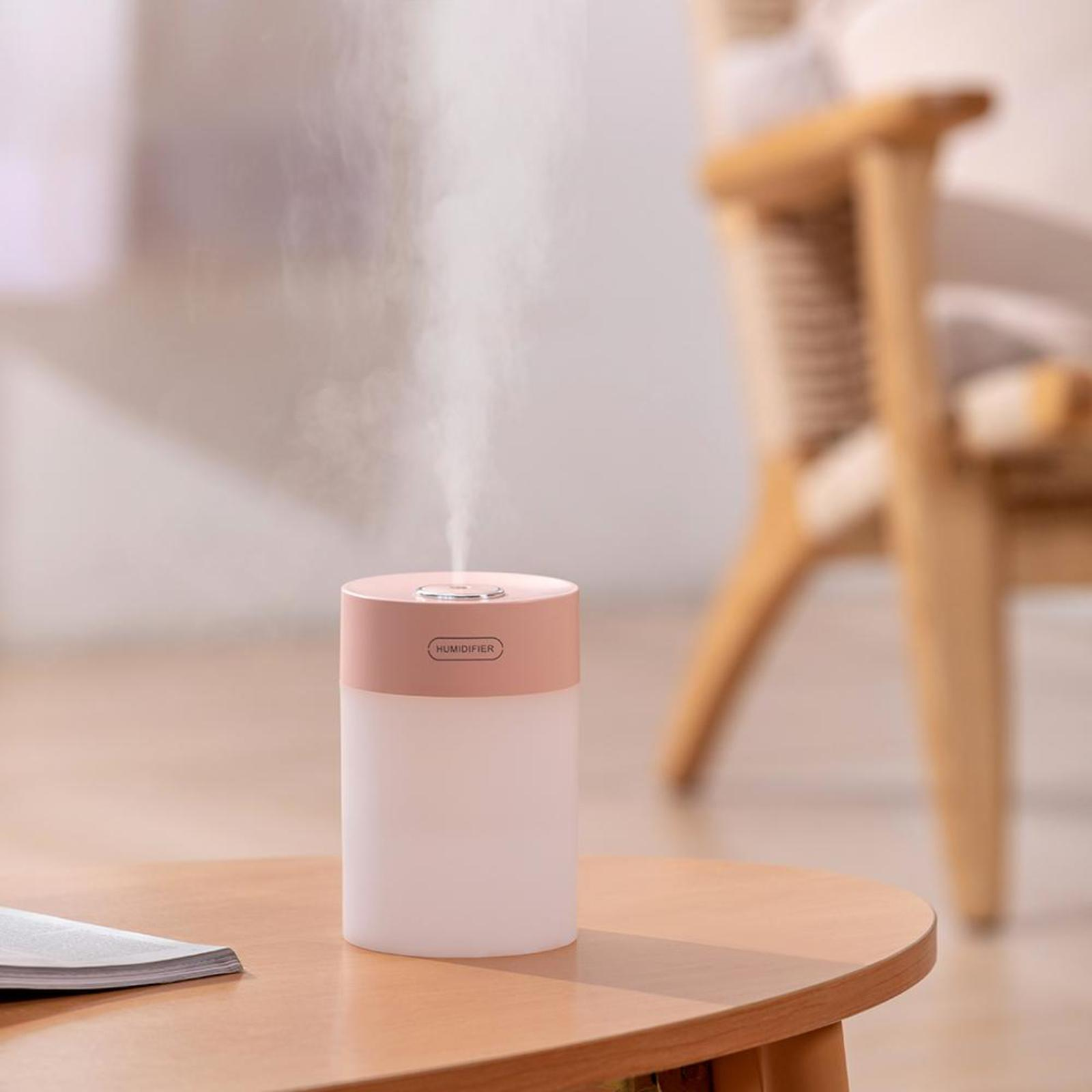 Ein weißer Luftbefeuchter mit rosa Deckel steht auf einem Holztisch und gibt Nebel ab. Ein verschwommener Hintergrund ist vorhanden.