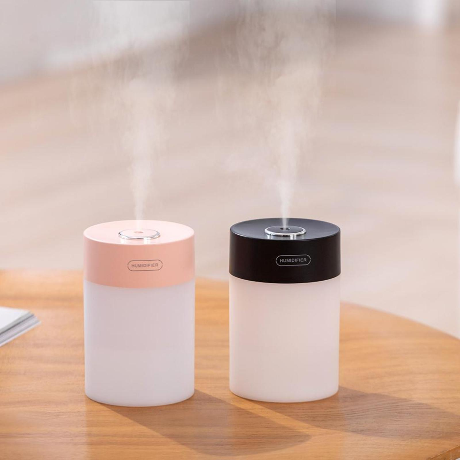 Zwei Luftbefeuchter, einer rosa und einer schwarz, stehen auf einem Tisch. Beide geben Nebel ab. Text hebt den Tank hervor.