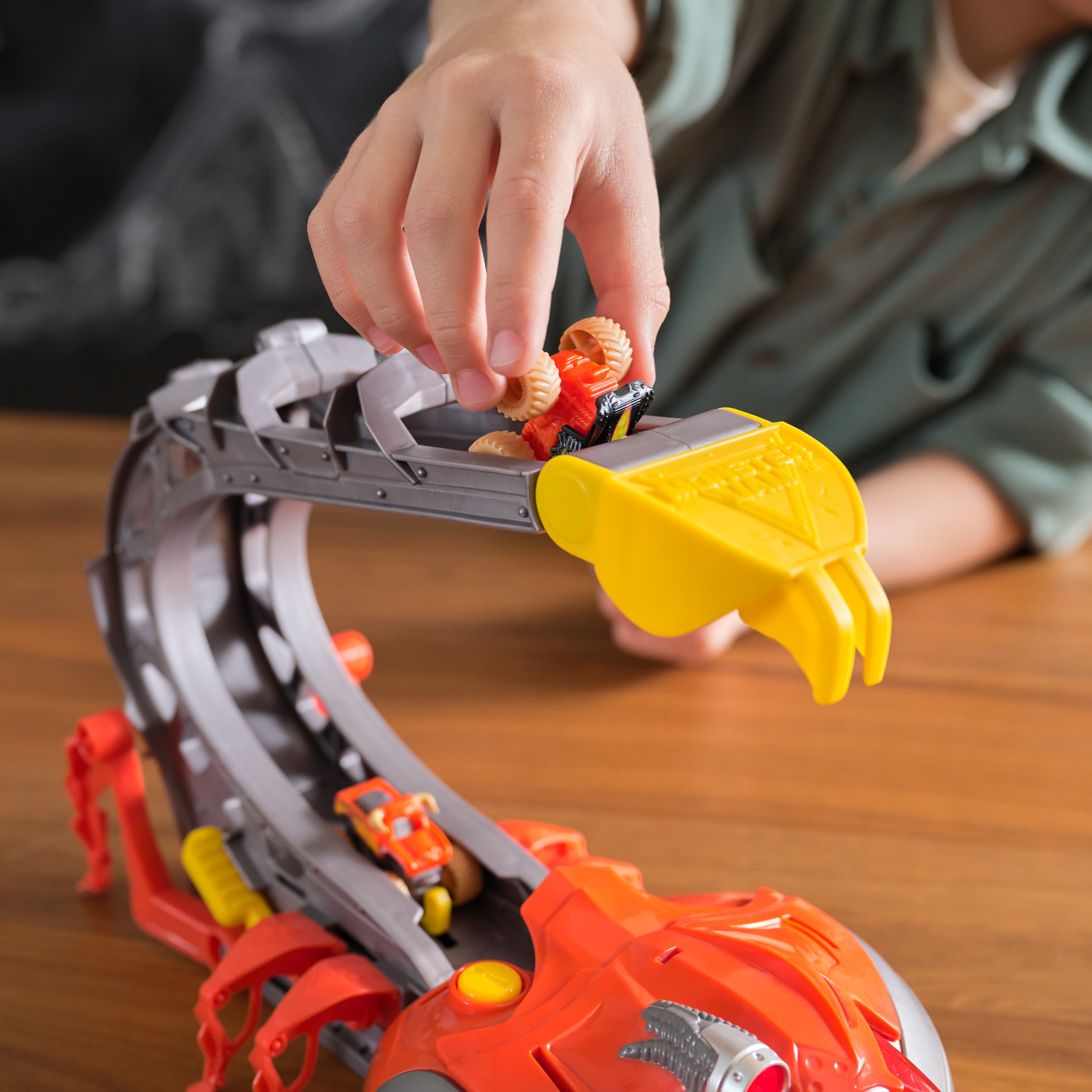 Ręka dziecka bawi się zestawem zabawek Monster Jam. Zestaw znajduje się na drewnianym stole.