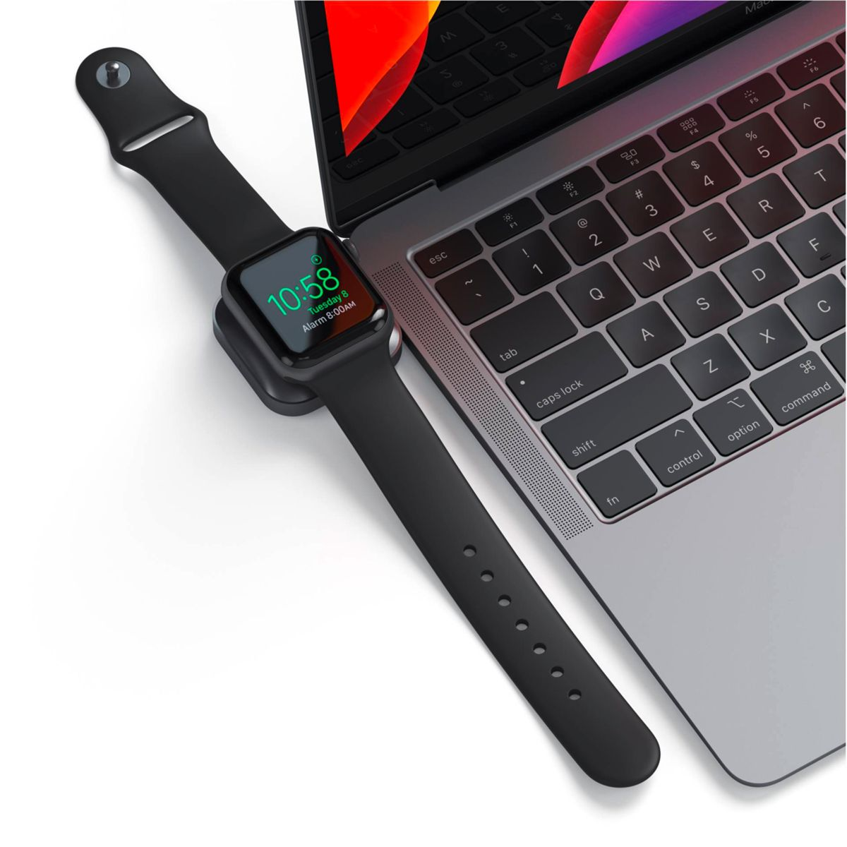Czarny Apple Watch na stacji ładującej obok laptopa. Zegarek wyświetla godzinę.