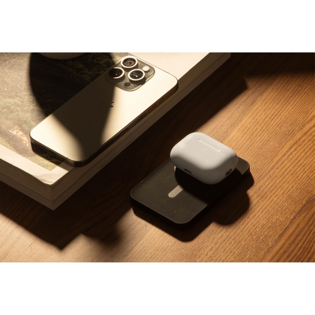 Un téléphone et des AirPods sur une surface en bois. Le téléphone est incliné, avec les AirPods sur un socle de chargement.