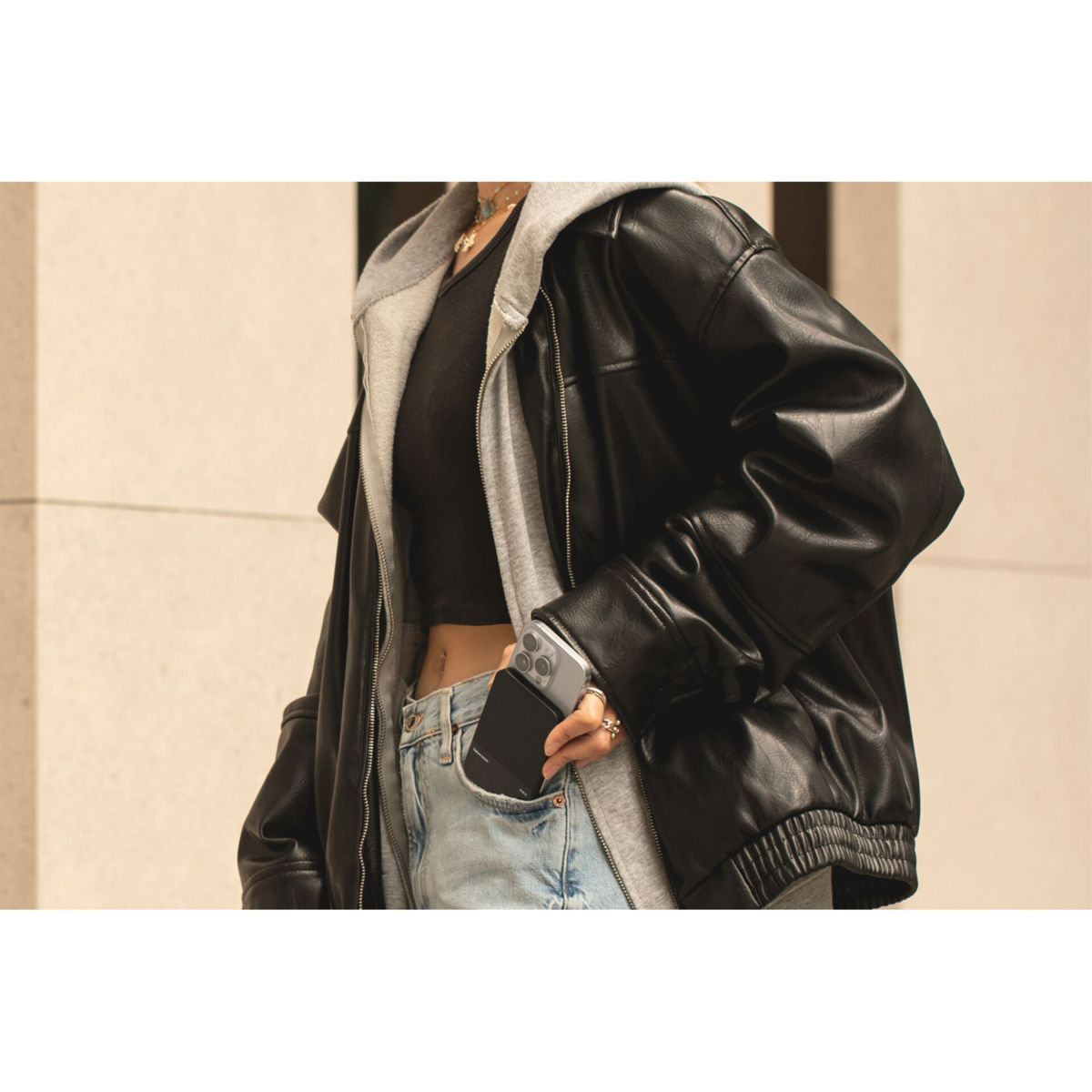 Une personne en veste noire avec un téléphone dans sa poche. Le téléphone est visible dans la poche. Fond clair.