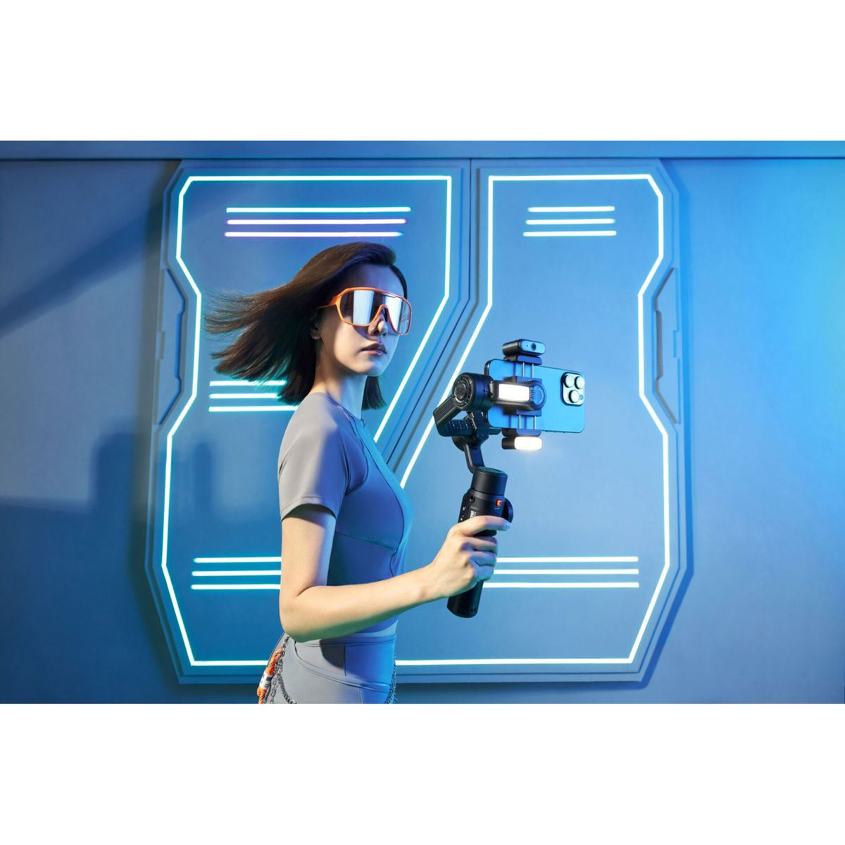 Eine Frau mit orangefarbener Brille hält ein Telefon auf einem Gimbal in futuristischer Umgebung, Neonlichter im Hintergrund.