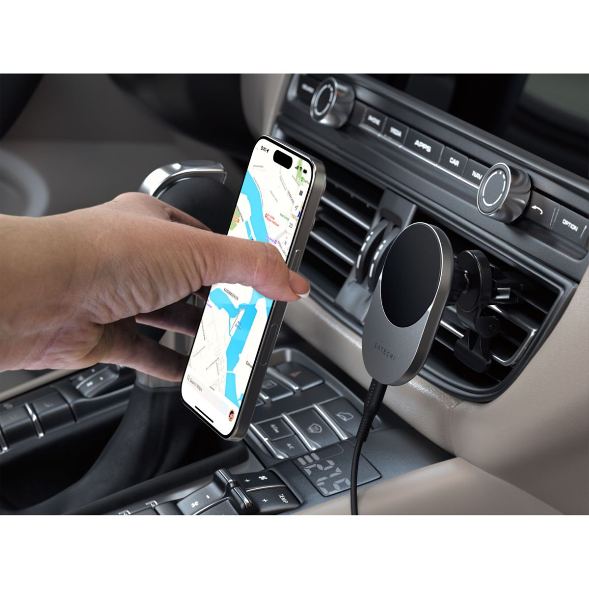 La mano de una persona sostiene un teléfono que muestra una aplicación de mapas, montado en una rejilla de ventilación del coche. El interior del coche es visible.