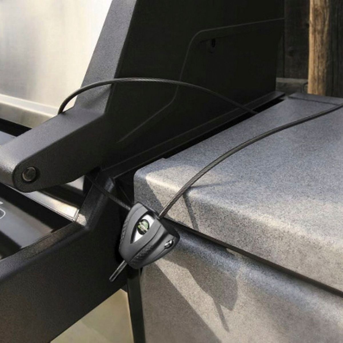 Ein schwarzes Schloss ist an einem Grill befestigt. Ein Kabel erstreckt sich vom Schloss. Das Schloss befindet sich auf einer grauen Oberfläche.