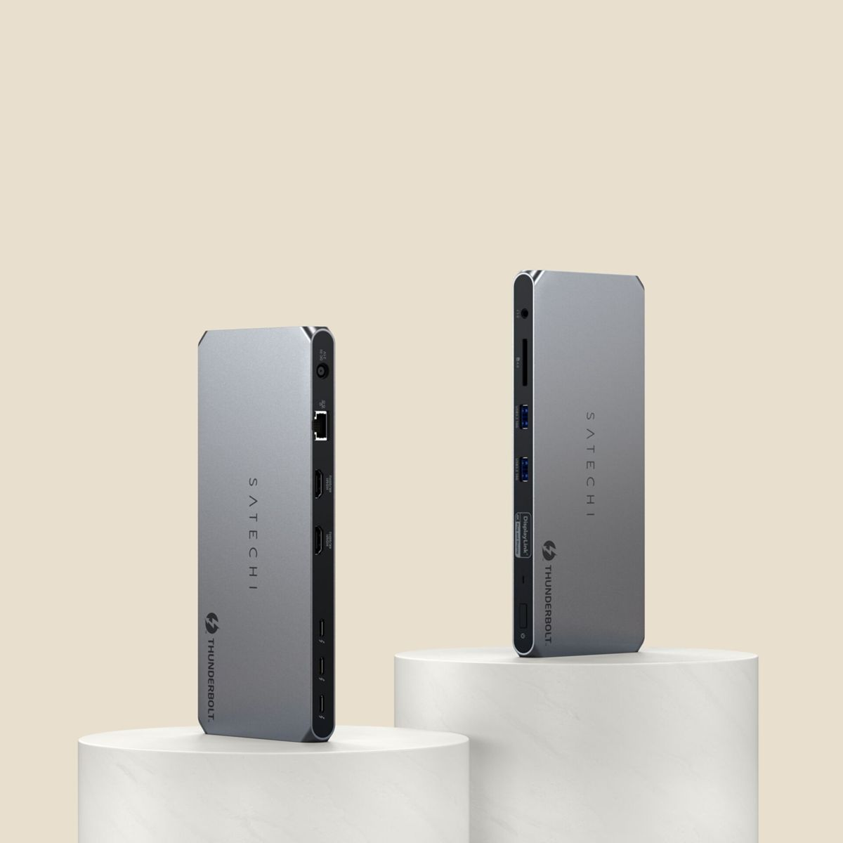 Zwei silberne Satechi Thunderbolt Hubs auf weißen Sockeln vor beigem Hintergrund.