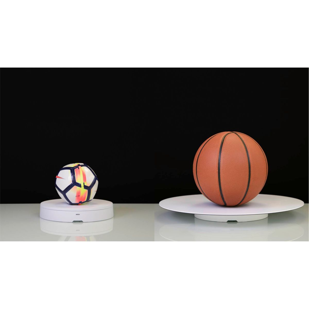 Un balón de fútbol y un baloncesto en exhibidores giratorios blancos separados, contra un fondo negro.