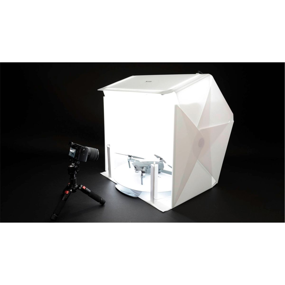 Un estudio fotográfico blanco con un dron dentro, una cámara en trípode en primer plano.