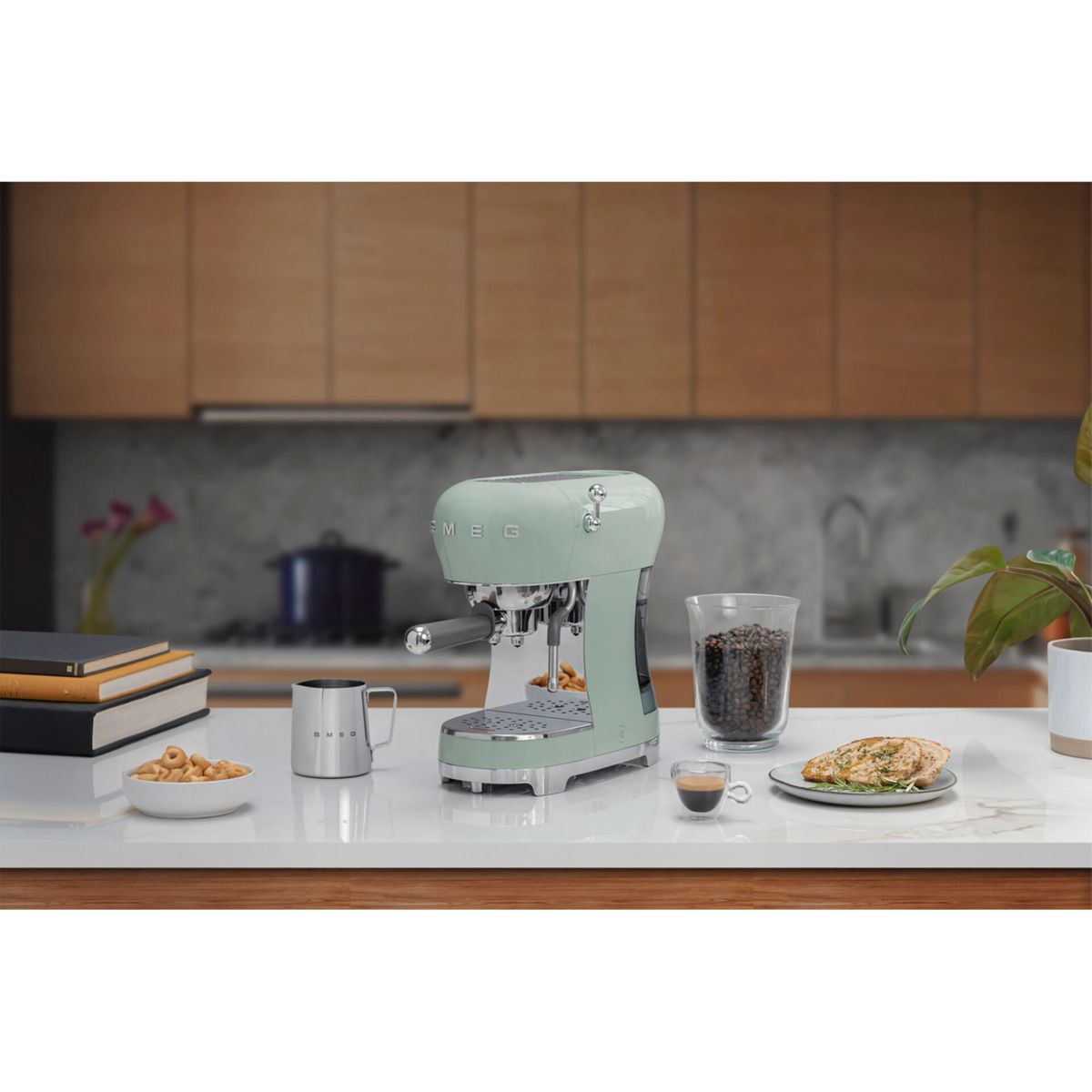 Máquina de espresso verde menta con tazas, granos y un plato de comida en una encimera blanca.