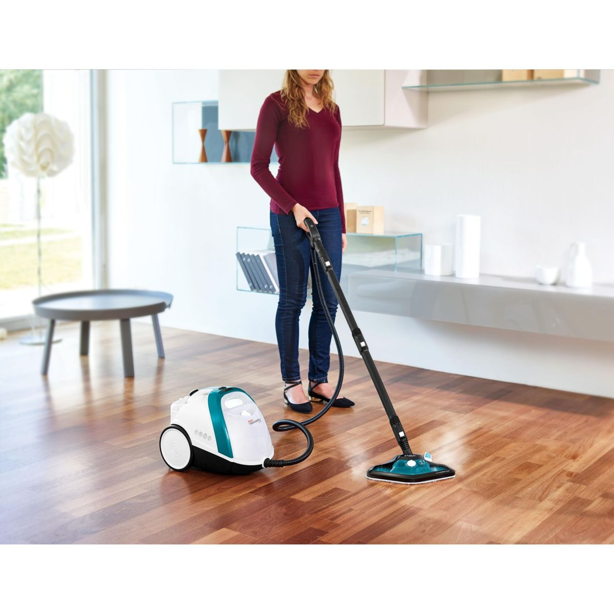 Kobieta czyści drewnianą podłogę myjką parową, białe i turkusowe urządzenie.