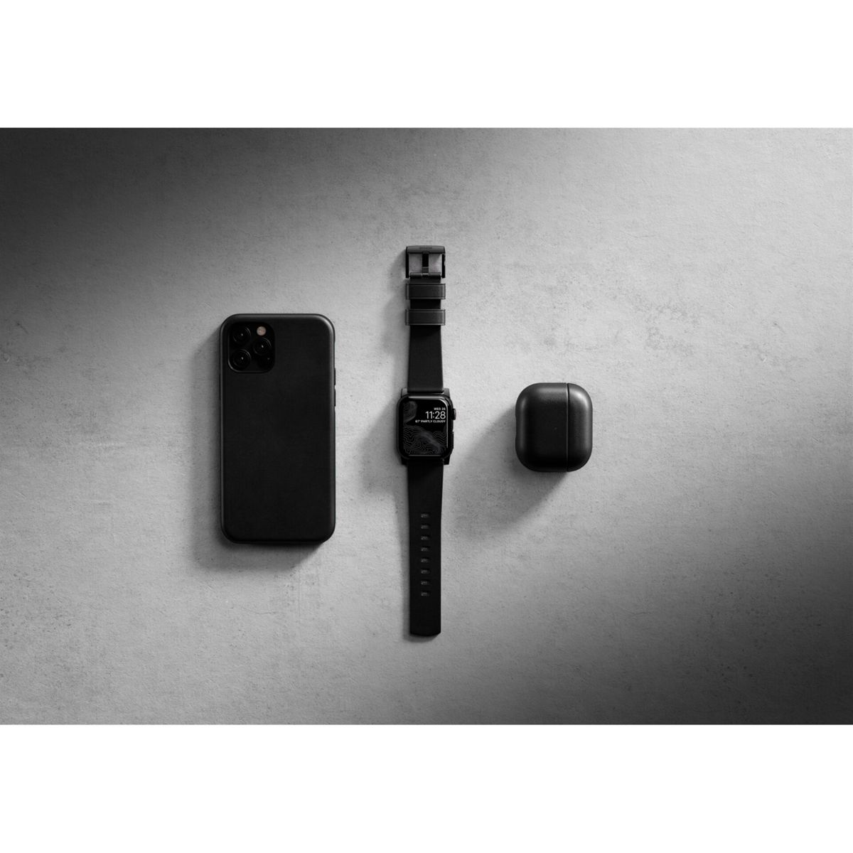 Telefono nero, orologio e custodia AirPods su una superficie grigia. L'orologio ha un cinturino nero. Vista dall'alto.