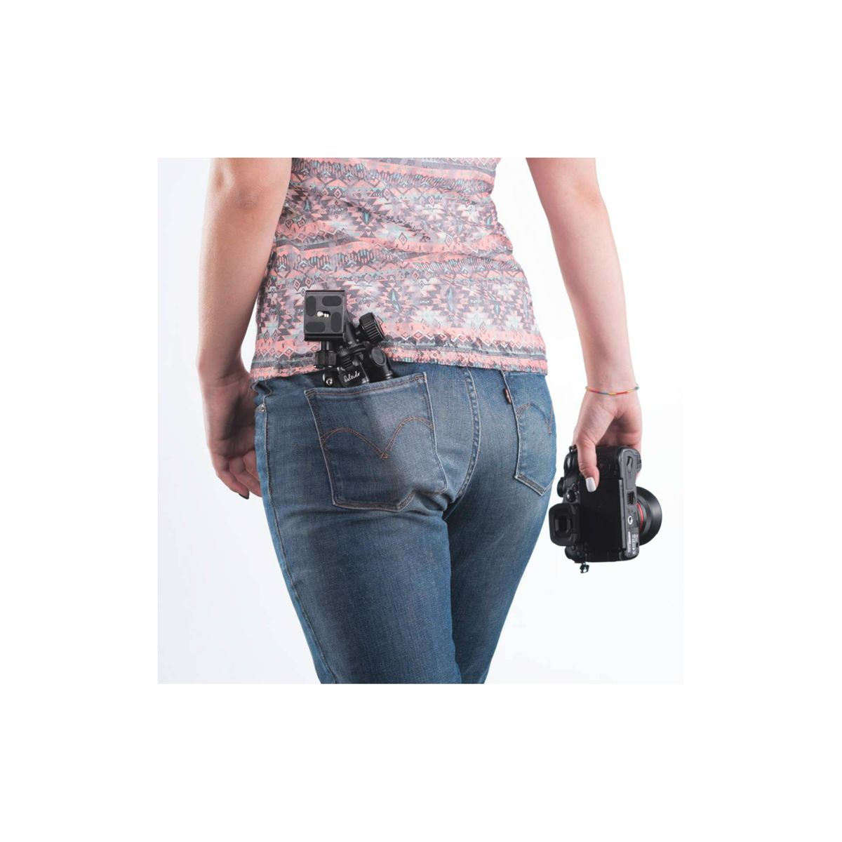 Una donna con jeans blu e una camicia a fantasia tiene in mano una macchina fotografica, un'altra in tasca.