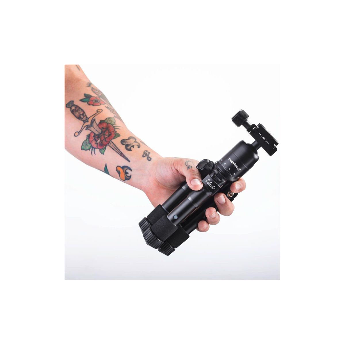 Una persona tiene in mano un treppiede nero, con un tatuaggio sul braccio.