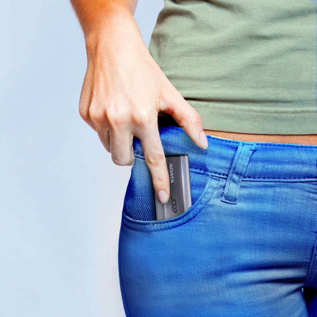 Dłoń kobiety wkłada szary dysk SSD do kieszeni niebieskich dżinsów, na białym tle.