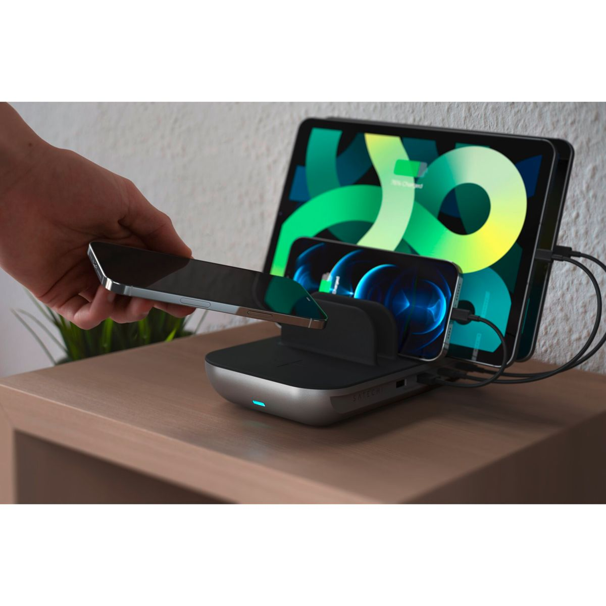 Eine Hand legt ein Telefon auf eine Ladestation neben einem Tablet und einem weiteren Telefon ab.