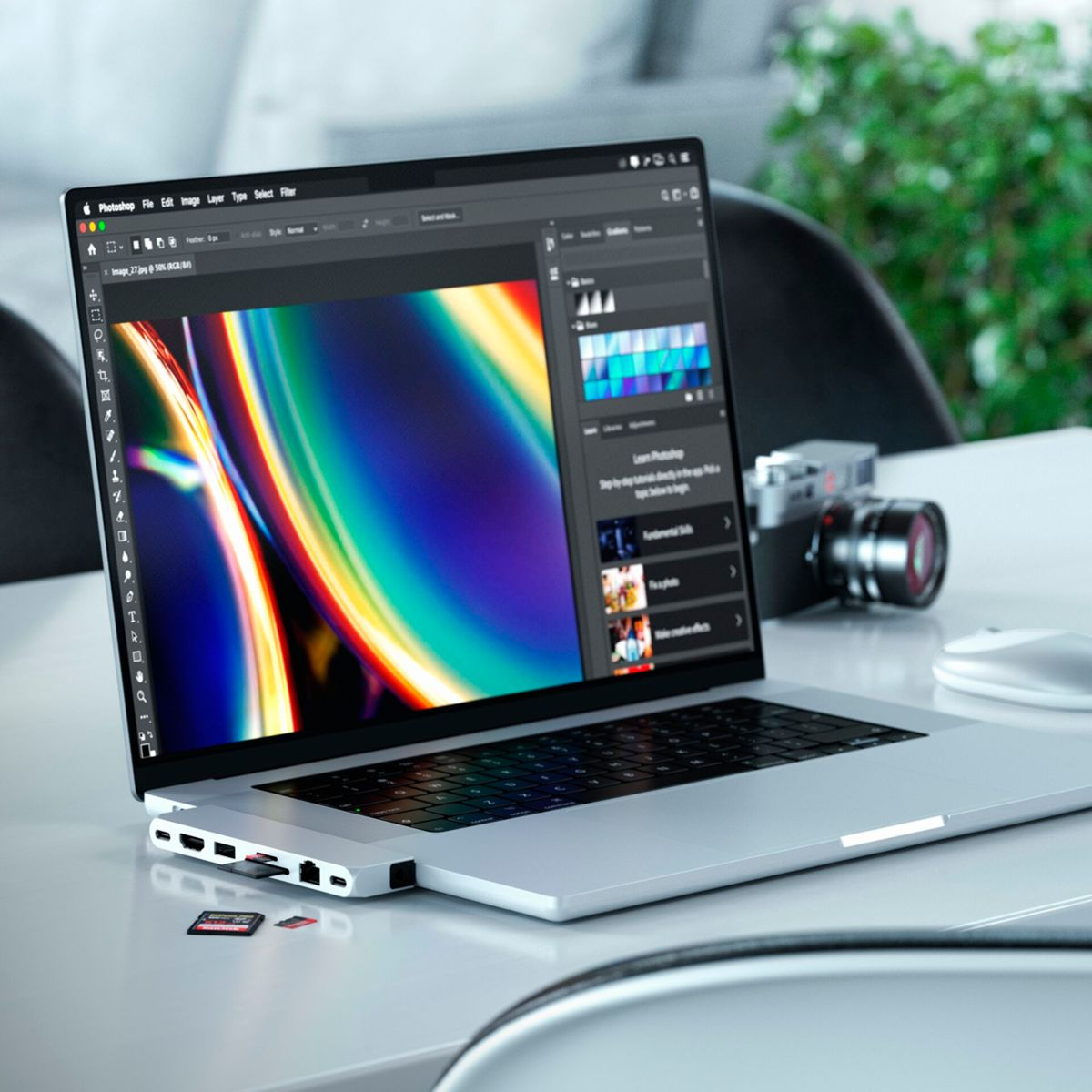 Laptop auf einem Tisch mit Kamera und Karten. Photoshop ist auf dem Display geöffnet.