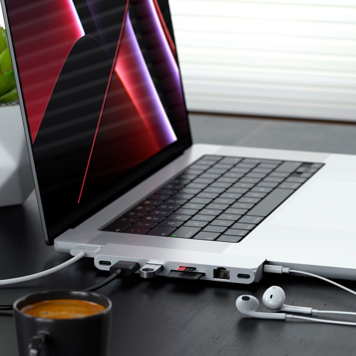 Laptop mit angeschlossenem Hub. Kaffeetasse und Kopfhörer sind im Vordergrund.