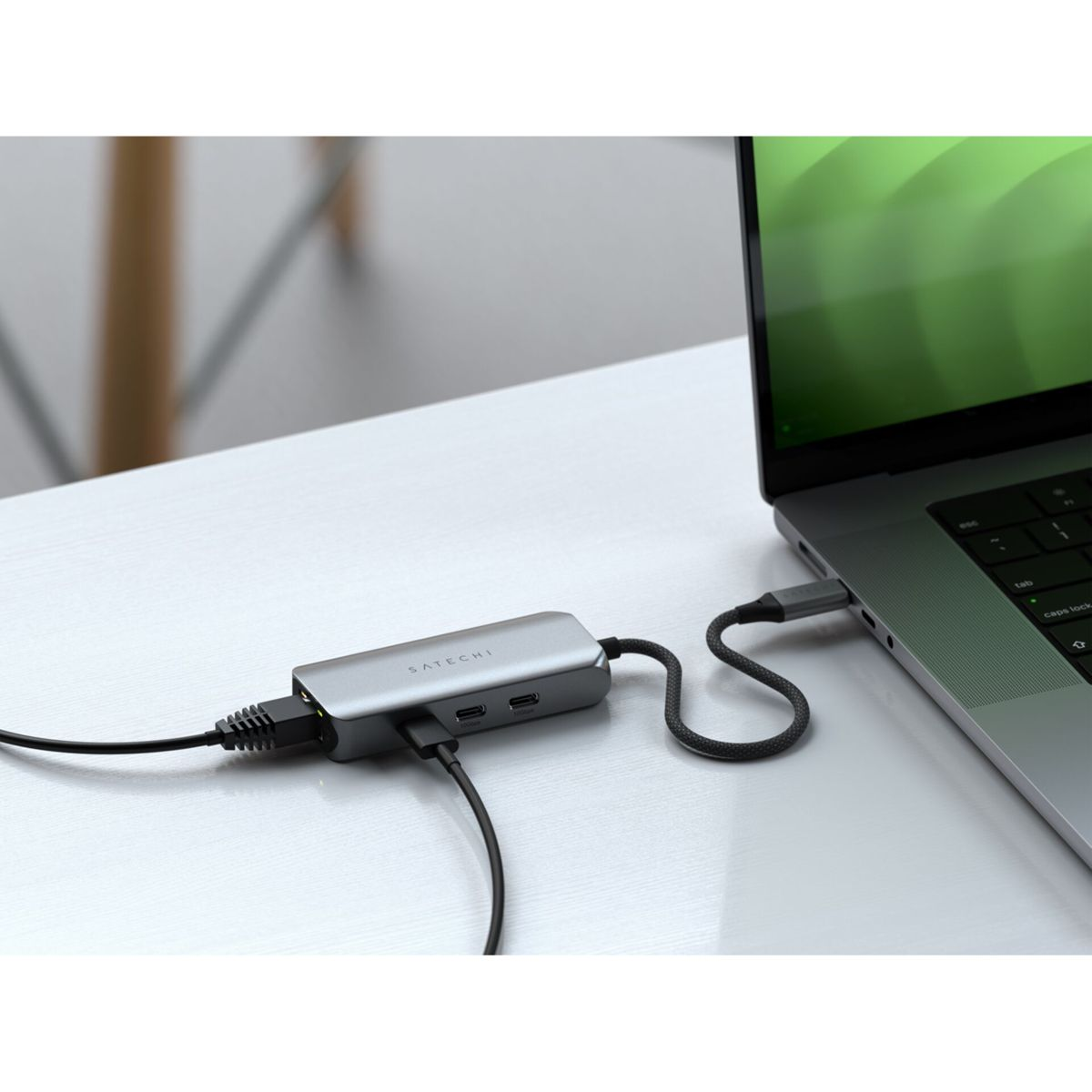 Ein Laptop, der mit einem silbernen Hub auf einem weißen Tisch verbunden ist. Der Hub hat mehrere Anschlüsse.