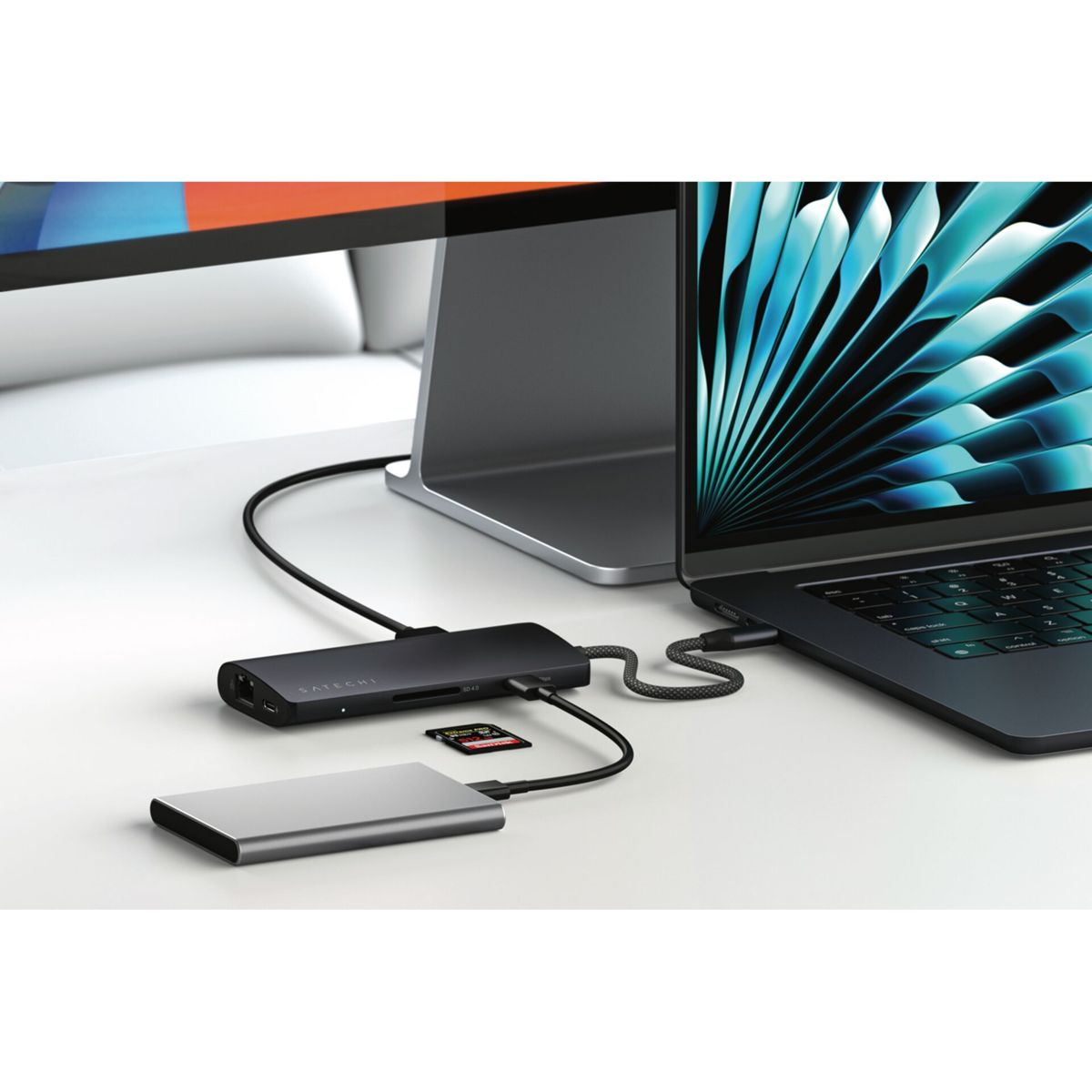 Un portátil con un concentrador conectado, con un disco duro y una tarjeta SD también conectados en un escritorio blanco.