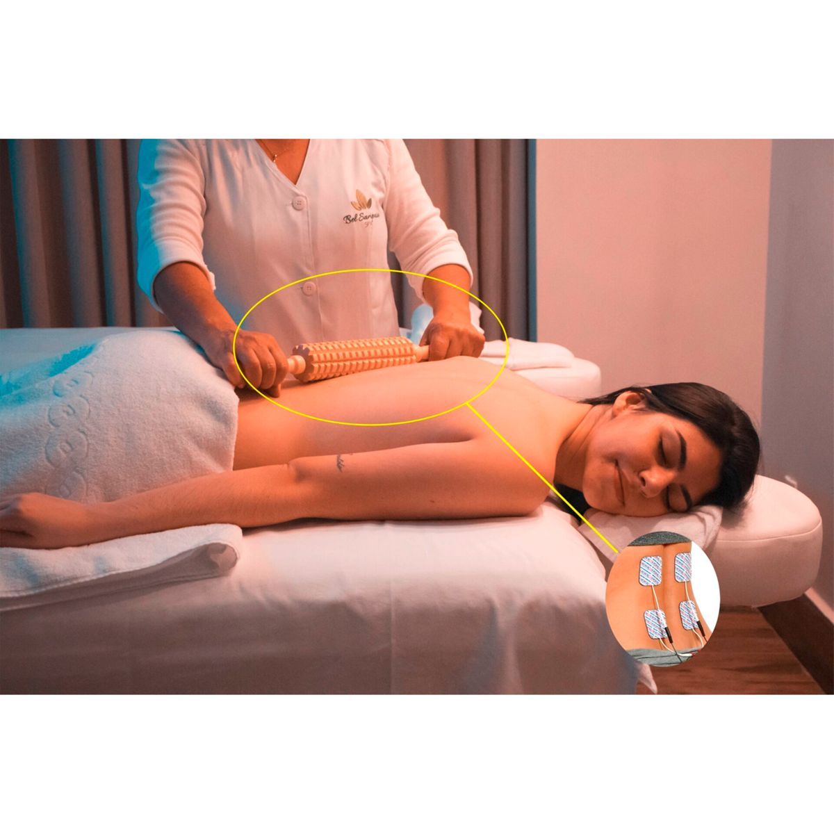 Frau liegt auf dem Bauch und bekommt eine Massage mit einer Holzrolle auf dem Rücken, mit Elektroden.