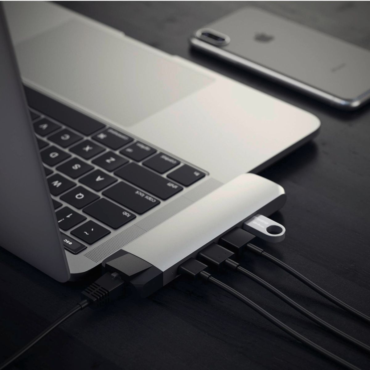 Un laptop con un hub collegato. Ci sono più cavi e un iPhone visibile.