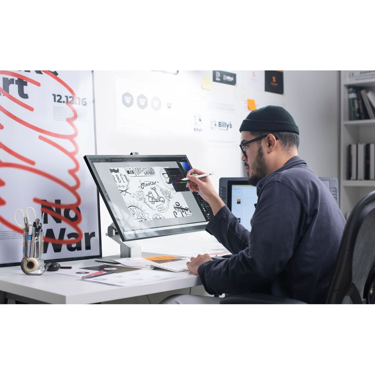 Une personne dessine sur une tablette numérique sur un bureau blanc.