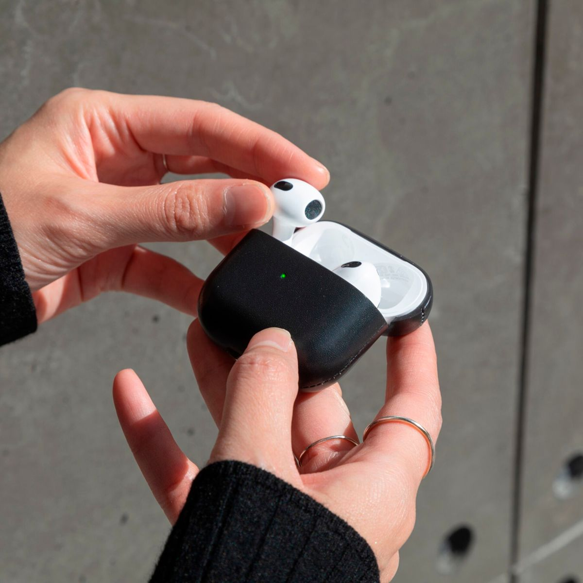 Les mains tiennent un étui AirPods noir ouvert avec des écouteurs blancs à l'intérieur.