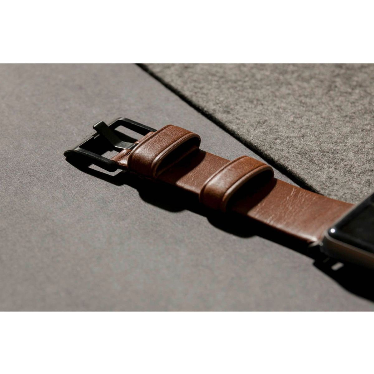 Nahaufnahme eines braunen Lederarmbands mit schwarzer Schnalle, das auf einer grauen Oberfläche liegt.