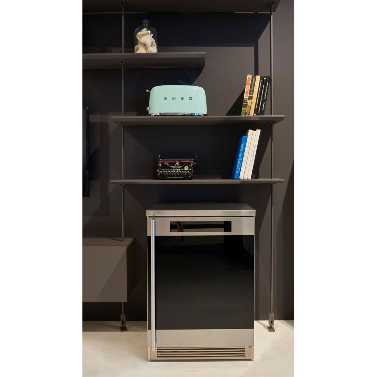 Ujęcie wnętrza z półkami trzymającymi toster, maszynę do pisania, książki i szafkę poniżej.