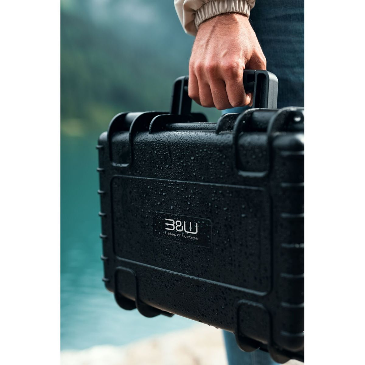 Eine Person hält eine schwarze B&W-Tasche vor einem See mit dem Wortlaut 'Cases of Success'.
