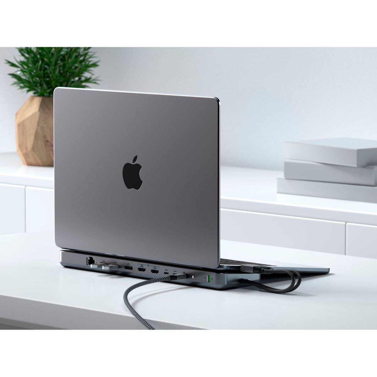 Un laptop su un hub con varie porte. Un quaderno e occhiali sulla scrivania.