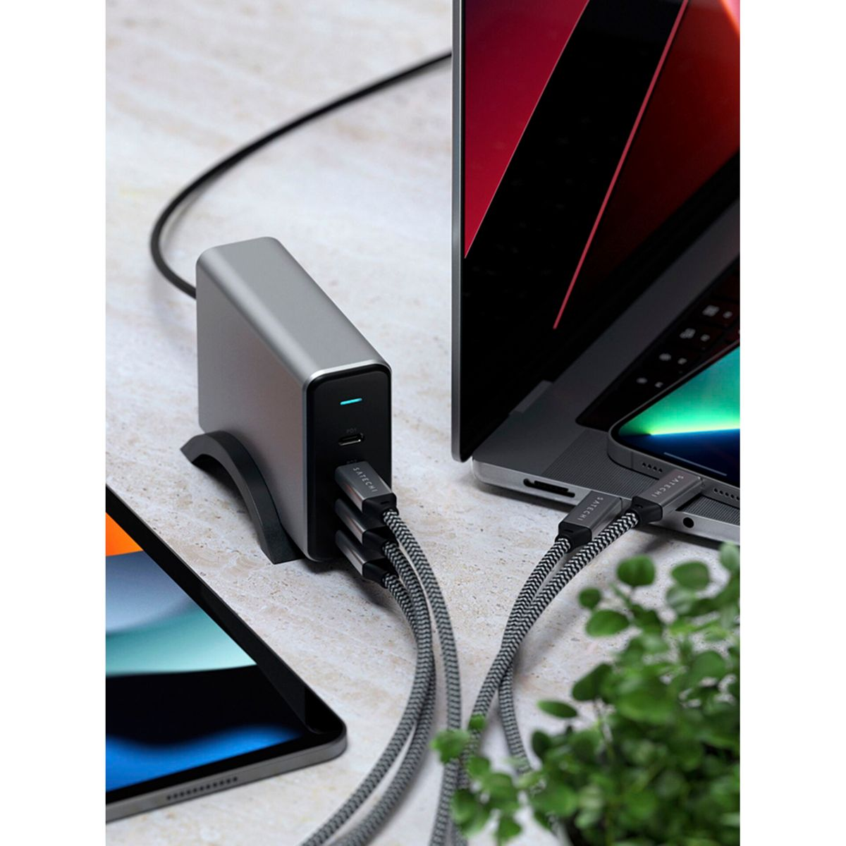 Una estación de carga plateada con cables conectados a una computadora portátil, un teléfono y una tableta.
