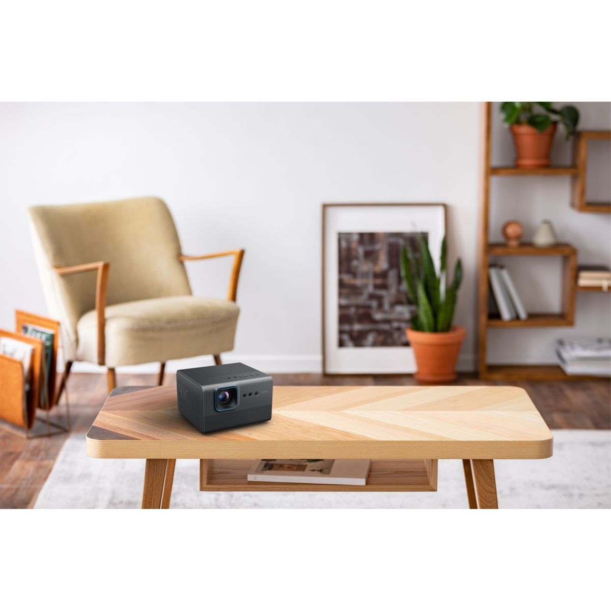 Czarny projektor na drewnianym stole. W tle widać beżowe krzesło i roślinę.