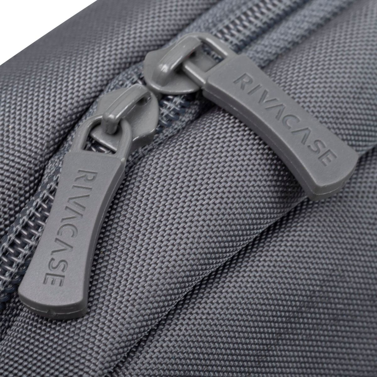 Zwei graue Reißverschlüsse mit RIVACASE-Etiketten auf einer grauen Tasche.