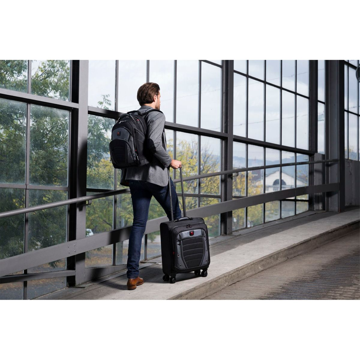 Ein Mann zieht einen schwarzen Koffer auf dem Bürgersteig, mit einem Rucksack auf dem Rücken.