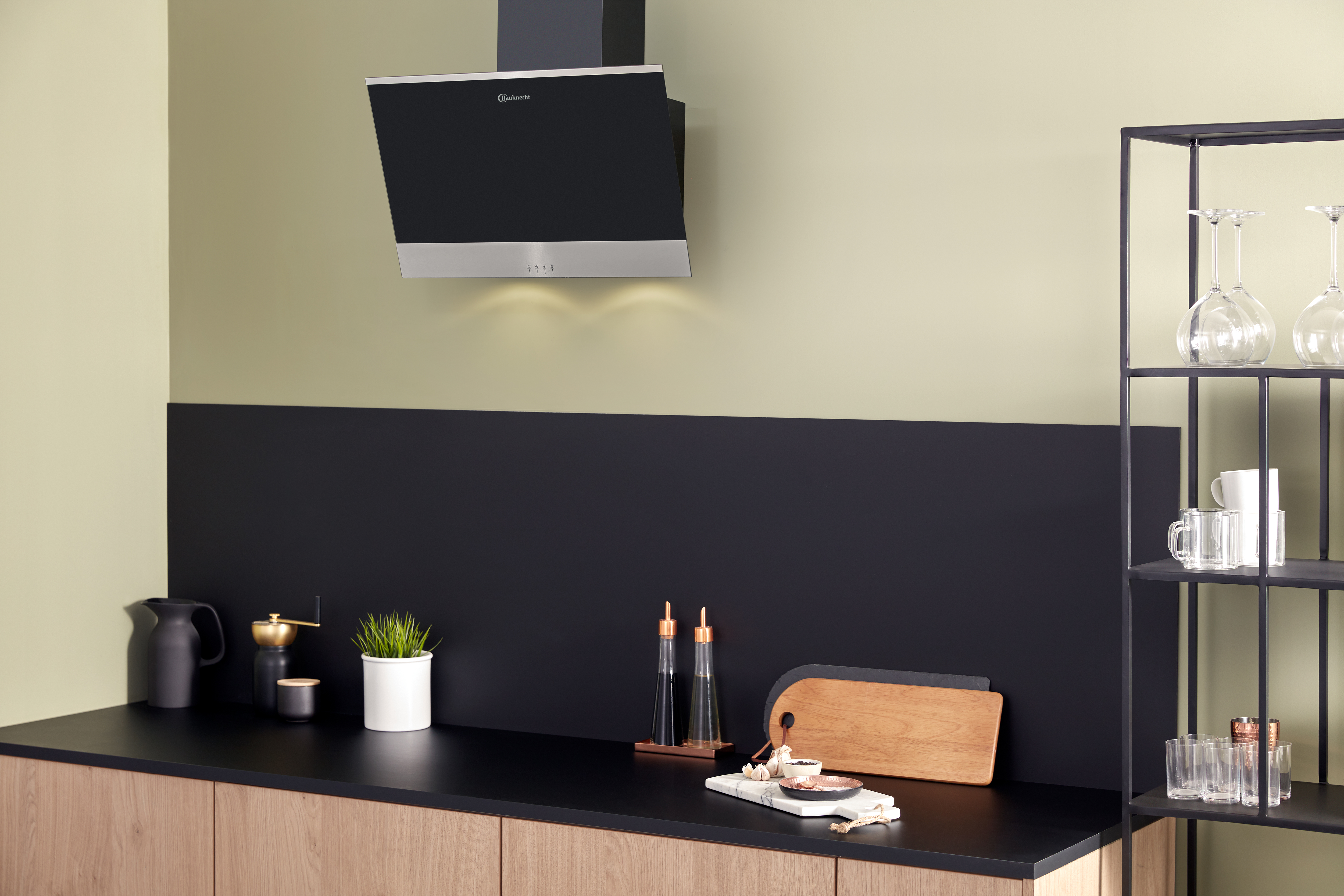 Una scena di cucina con una cappa nera, un piano di lavoro nero e mobili in legno. Sono presenti vari oggetti da cucina.