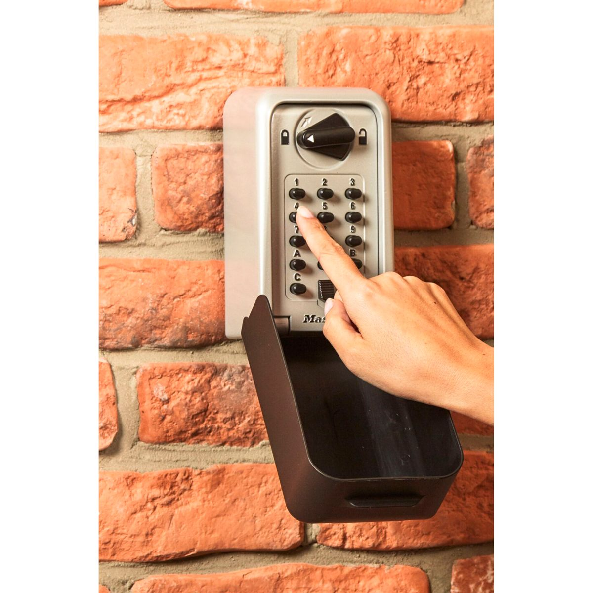 Eine Hand drückt eine Nummer auf einem Zahlenschloss-Schlüsselkasten an einer Backsteinmauer.