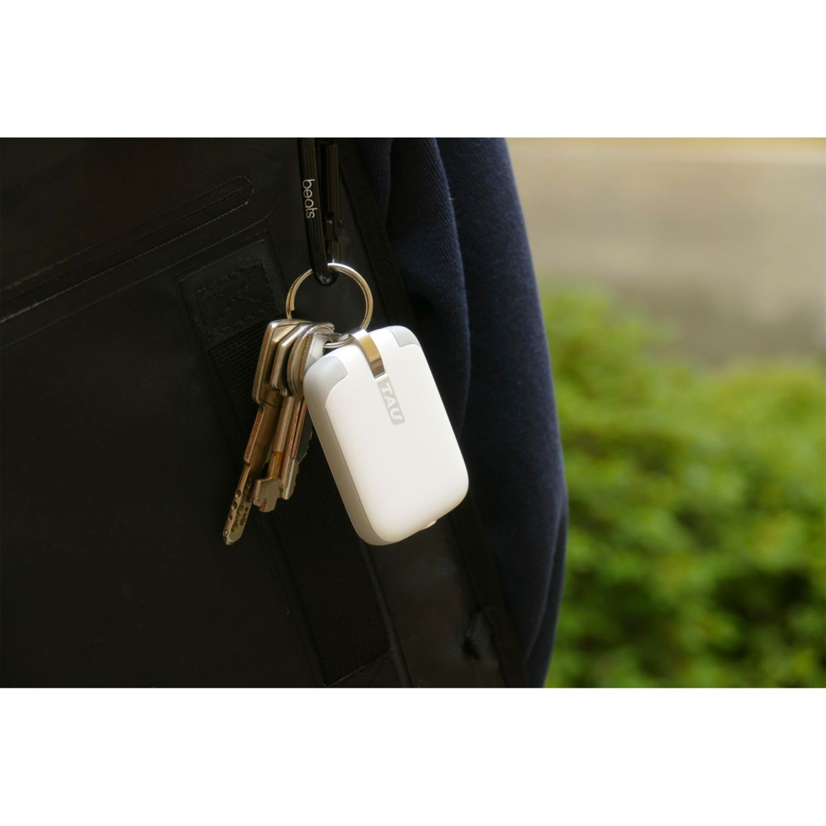 Un porte-clés avec un appareil de chargement blanc. Il est attaché à des clés et à une sangle noire.