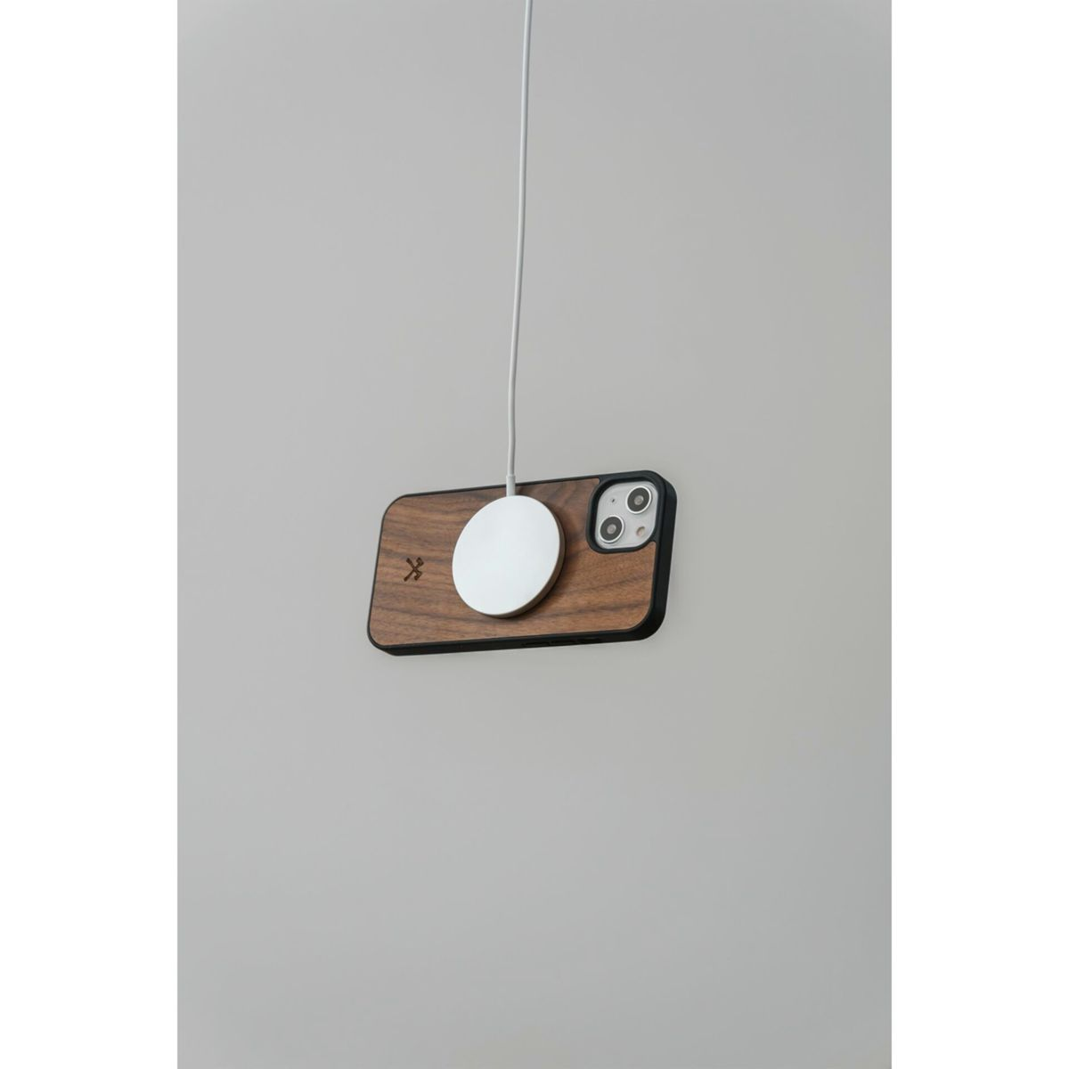 Ein Telefon in einer Holzschutzhülle, mit einem weißen Ladegerät auf der Rückseite, das in der Luft hängt.