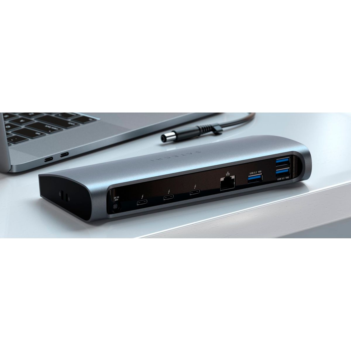 Ein silbernes Gerät mit mehreren Anschlüssen, ein Laptop und ein Kabel auf einem weißen Schreibtisch.