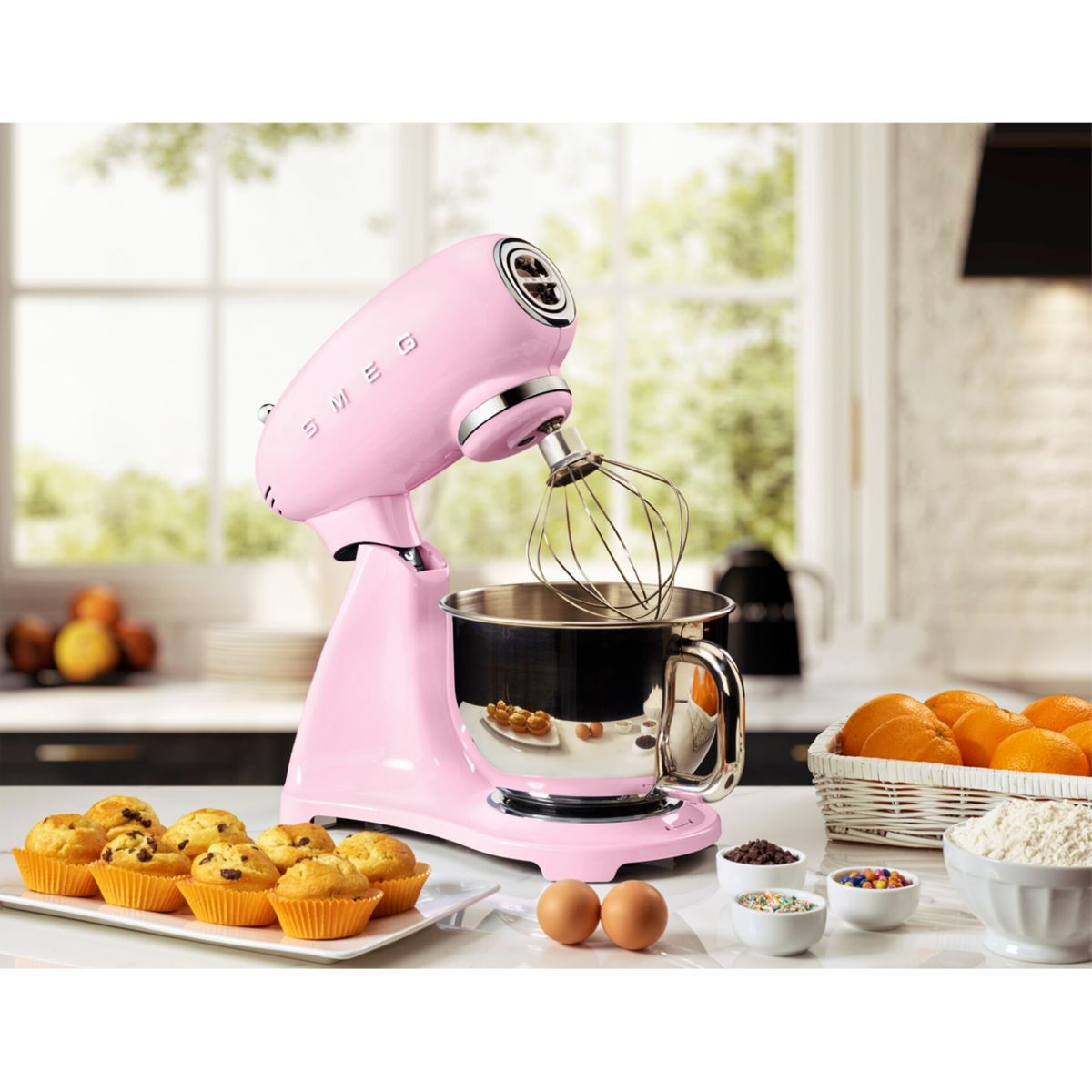 Paslanmaz çelik bir kase, kekler ve bir tezgahta malzemelerle pembe bir SMEG mikser.