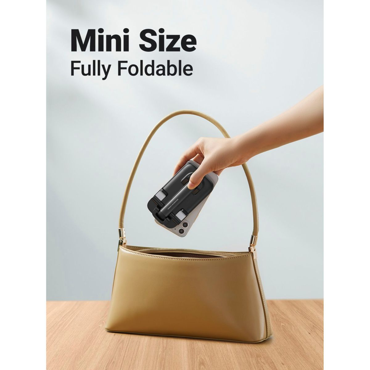 Dłoń umieszcza złożone czarne urządzenie w beżowej torebce. Urządzenie jest oznaczone 'Mini Size Fully Foldable'.
