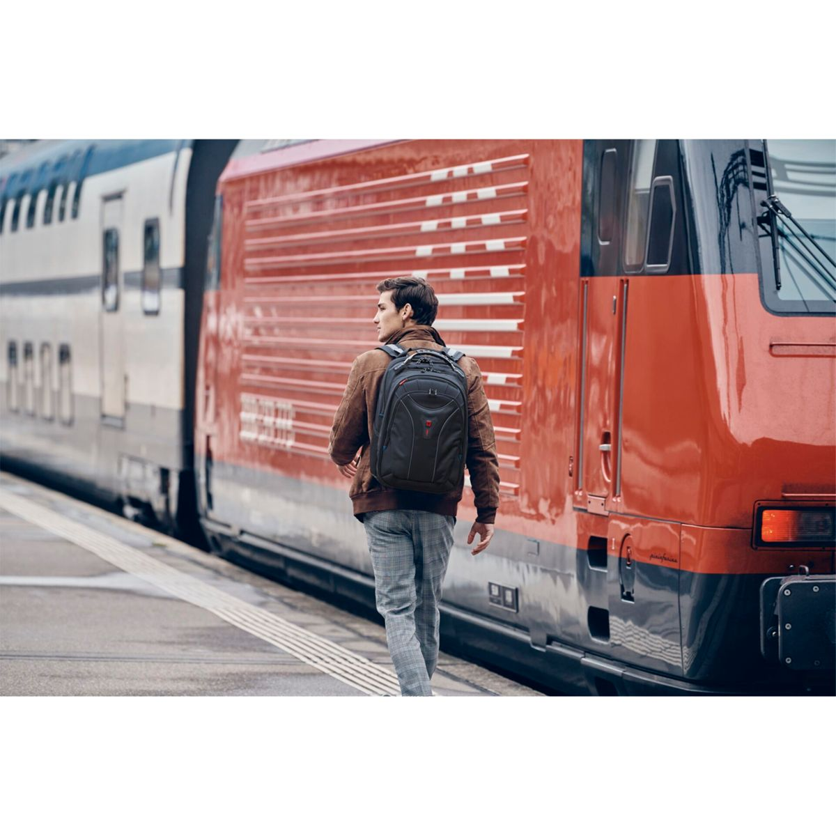 Ein Mann mit Rucksack geht auf einem Bahnsteig auf einen Zug zu. Ein rot-weißer Zug befindet sich auf der rechten Seite.