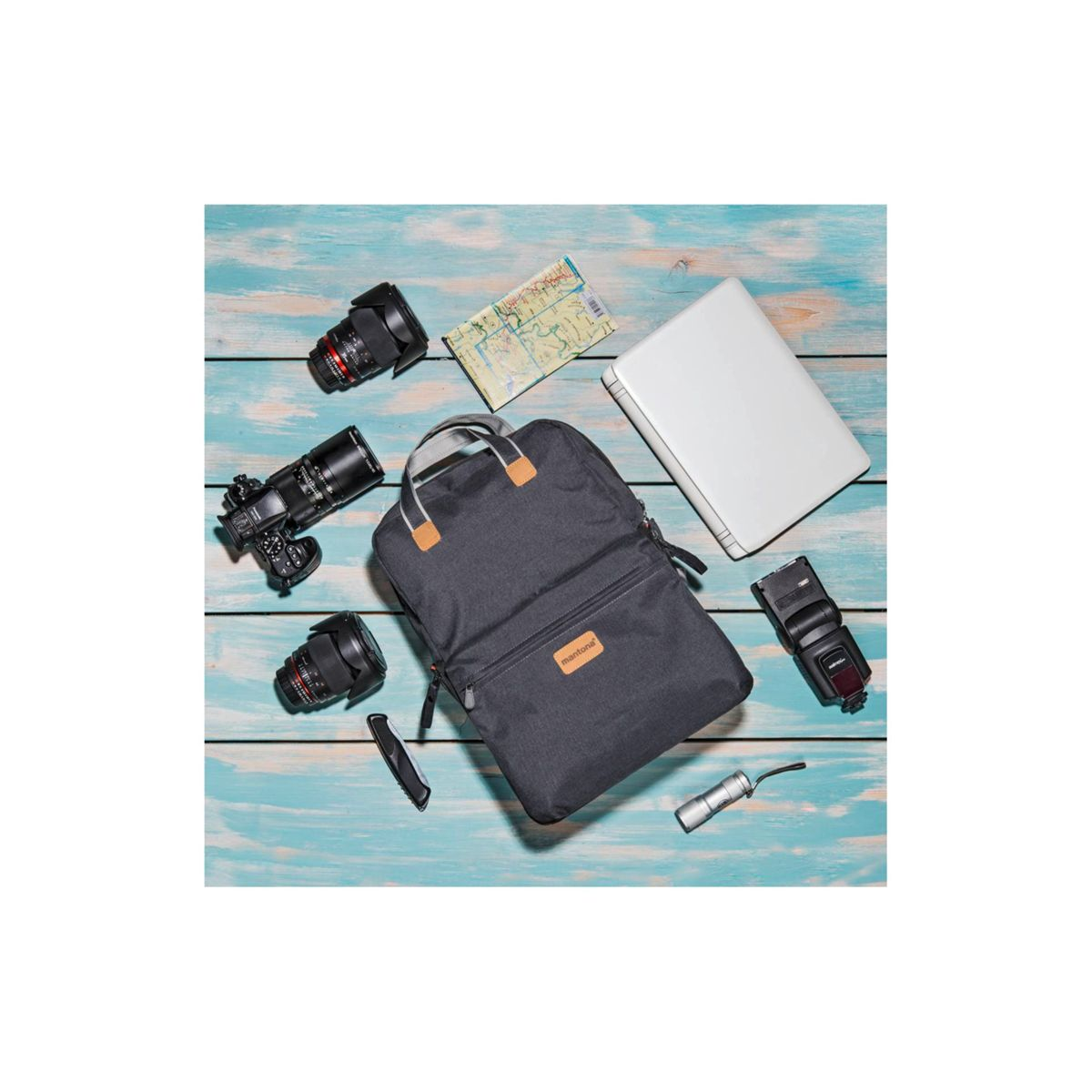 Ein Rucksack mit Kameraausrüstung auf einer blauen Holzoberfläche: Objektive, Kamera, Blitz, Karte, Laptop.